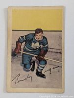 Front side of the hockey card showing illustration of Rudy Migay in Toronto Maple Leafs uniform on ice.