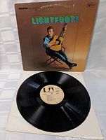 Vinyl LP record laid out with cover behind it showing label and record surface.