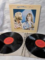 Two black vinyl records with red labels partially out of white paper sleeves along with album cover against white background