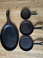 Top view showing all four cast iron pans arranged on a wooden surface: one large oval pan and three smaller round pans.