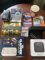 Photo showing all items arranged on a wooden table including timer, Apple TV mount, candle clapper, Tommy Hilfiger wallet, door lock, power strip, coffee pod holder, and other gadgets.