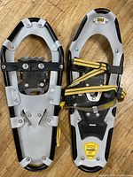 Pair of Atlas Series snowshoes with aluminum frames, black and yellow straps, and serrated crampons visible.