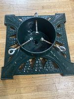Top view of a green cast iron Christmas tree stand with decorative patterns and three securing bolts.