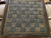 Close-up image of the carved chessboard showing intricate glyph designs on each square, and decorative carved border.