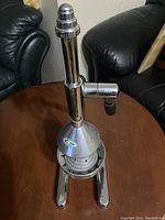 Full side view of commercial manual juice presser on table with black leather chairs in background.