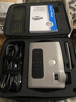 Dell 3400MP projector inside a black carrying case along with power cable, VGA cable, remote control, and owner's manual.