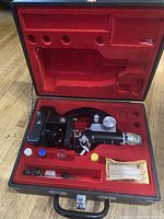 Open carrying case revealing Easton's Optima microscope with multiple accessories and filter disks inside red velvet-lined compartments.