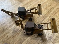 Photo showing two yellow Ertl backhoe construction toys side by side on wooden floor.