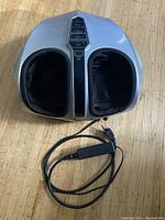 Silver electric foot massager machine with cushioned foot chambers and control buttons on top, including power adapter and cord.