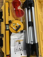 Photo showing laser level device, tripod, yellow level, red glasses, and instruction manual inside yellow case.