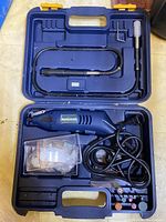 Blue plastic case open showing the Mastercraft rotary tool, flexible shaft attachment, power cord, and multiple sanding/grinding accessories in separate compartments.