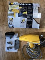 Photo of the yellow handheld steam cleaner with six attachments laid out alongside the worn McCullough original box and instruction sheet.