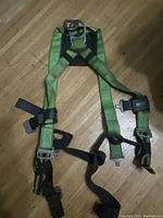 Full view of green Miller safety harness showing adjustable straps and metal buckles on wooden floor.