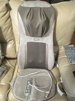 View of the massage cushion showing beige and brown fabric with padded segments and attached wired remote control on couch seat