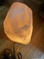 Illuminated salt rock lamp on a wooden surface showing its natural, rough texture and warm amber light.