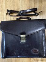 Closed view of dark brown leather briefcase bag with flap and metal clasp lock showing Bugatti embossed logo