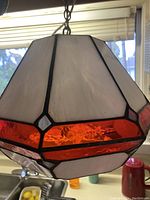 Close-up of the stained glass chandelier showing white opaque glass panels with a textured red glass band near the middle, framed with black metal.