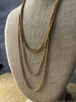 Front view of the three strand gold-toned necklace displayed on a fabric bust showing the layered strands.