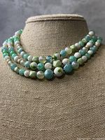 Front view of the vintage multi-strand green and white bead necklace on display bust.