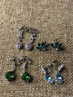 Four pairs of sterling silver clip-on earrings with different colored crystals displayed on a tan fabric background.