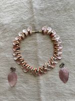 Photo showing full blush cut conch shell necklace laid flat with the pair of blush pink leaf clip-on earrings placed beside it for display.