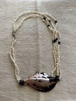 Full view of the necklace showing the carved abalone shell pendant and torsade style beading with white and coral beads.