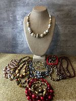 Photo of mannequin bust displaying a large wooden bead necklace and a spread of multiple assorted bead necklaces in front on burlap surface