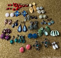 Top-down view of the entire large lot of vintage earrings showing various colors and styles on a textured brown surface.