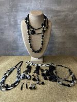 Full lot including necklaces displayed on bust and laid out jewelry pieces including earrings and bracelets on burlap surface.