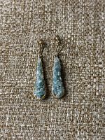 Front view of the pair of vintage jadite green textured teardrop earrings with gold-tone metal framing and screw-back clip closure, placed on a textured fabric background.
