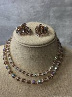 Photo showing the lavender crystal necklace and matching clip-on earrings displayed on a linen bust stand against a gray background.