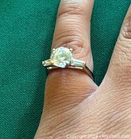 Close-up of ring worn on finger showing large round clear stone and two tapered baguette stones on sides