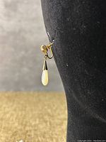 Side view of one earring clipped on a display, showing teardrop mother of pearl dangler and clip mechanism.