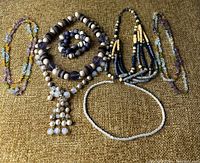 Wide shot showing entire lot of six necklaces and one bracelet laid out on fabric background.