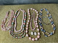 Four necklaces predominantly pink and one pair of matching clip-on earrings laid flat on green fabric.