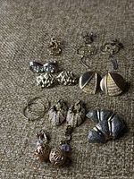 Eight pairs of vintage earrings laid out on fabric background showing variety in style and metal tones.