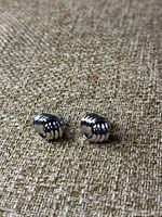 Pair of silver-tone earrings with ribbed curved design on textured fabric background.