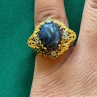 Close-up photo of the vintage ring on finger showing central blue star sapphire in gold filigree with accent stones.