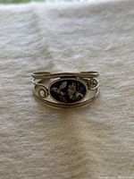 Front view of sterling silver cuff bracelet with oval abalone shell inlay and swirl accents, displayed on white fabric.