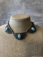 Front view of vintage silver tone filigree bib choker with turquoise color stones on display bust.