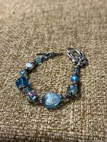 Bracelet with multi-shaped and colored glass beads including heart-shaped and faceted beads on a textured background.