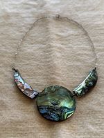 Front view of vintage abalone shell necklace showing iridescent green-blue round and crescent-shaped shell pendants on silver chain.