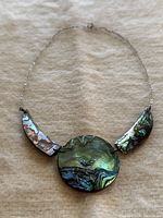 Overall view of the vintage abalone shell necklace showing the central round abalone piece and two crescent-shaped abalone shell segments on either side connected by a delicate silver chain.