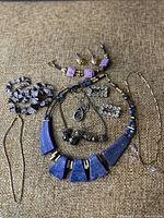 Overall view of the jewelry lot showing necklace, earrings, shoe buckles, bracelet, and necklaces on a brown fabric surface.