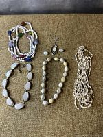 Lot of five assorted white-tone vintage style necklaces or bracelets laid out on a brownish textured fabric background.