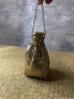 Front view of the small gold-tone metal mesh bag hanging from a short chain strap.