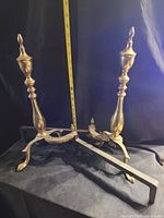 Two brass andirons shown with measuring tape indicating height around 22 inches.