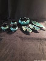 Seven Blue Mountain Pottery items displayed on black cloth background, showing overall collection and glaze colors.