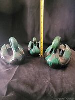 Three green glazed ceramic swan figurines shown with a ruler for scale, arranged on dark fabric background.
