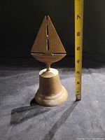 Brass sailboat bell standing next to a measuring tape about 7 inches tall.